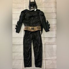 a batman costume on display in front of a white wall with wood planks behind it