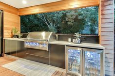 an outdoor kitchen with stainless steel appliances and wood paneling, along with large windows that look out onto the backyard