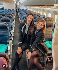 two women sitting on seats in an airplane with their backs turned to the side, smiling at the camera