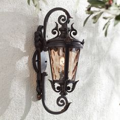 an old fashioned wall light on the side of a white building with green leaves hanging from it's sides