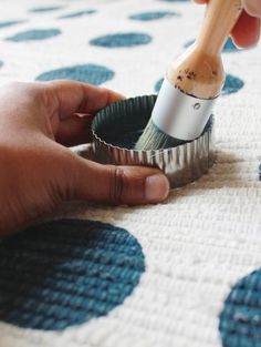 someone is using a brush to paint the inside of a cupcake tin on a polka dot tablecloth