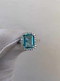 a ring with an emerald colored stone surrounded by small white diamond halos on top