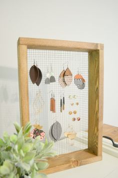 a wooden frame with earrings hanging on it and a potted plant next to it