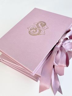 a pink book with a ribbon tied around the front and back cover that has a monogram on it