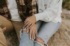 two people sitting on rocks with one holding the other's hand and wearing rings