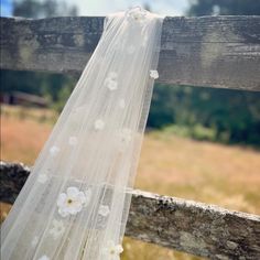 a white wedding veil hanging on a wooden fence in front of a field with flowers