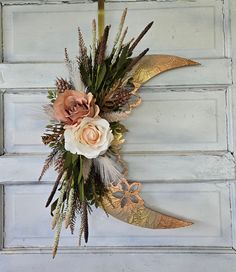 a wreath with flowers and feathers hanging on a door handle in the shape of a crescent