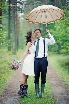 a bride and groom kissing under an umbrella in the rain on a path surrounded by trees