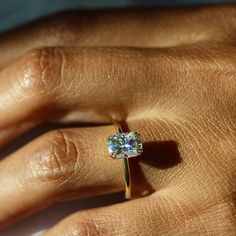 a person's hand holding a ring with a diamond on it and the middle finger