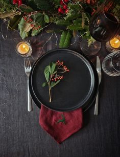 a black plate topped with a leafy plant next to a red napkin and candles