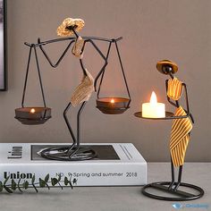 a statue of two people holding scales on top of a book next to a candle