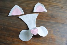 three pieces of felt with pink and white ears on top of a wooden table next to a pair of scissors