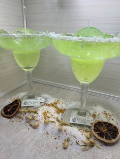 two margaritas sitting on top of a counter next to an orange peel and spices