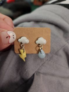 a pair of earrings with clouds, lightning and stars on them in front of a person's hand