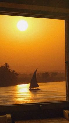 a sailboat is seen through the window of a dining room at sunset or dawn