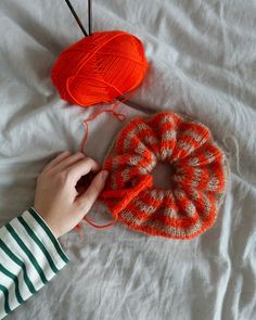 two balls of yarn sitting on top of a bed next to an orange knitted object