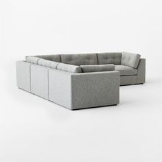 a gray sectional couch sitting on top of a white floor next to a grey ottoman