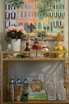 a bar cart filled with liquor bottles and glasses next to a painting on the wall