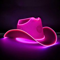 a pink cowboy hat sitting on top of a purple light under a black background,