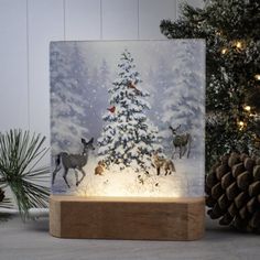 a lighted christmas tree with deer and birds on it in front of a pine tree