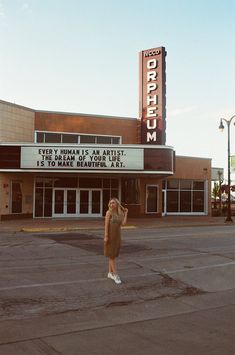 a woman standing in front of a theater with her hand up to the side of the building