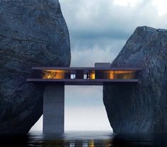 two people standing on a bridge over water with large rocks in the foreground and dark clouds above