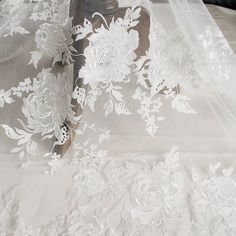 white lace with flowers on it sitting on top of a table cloth next to a suitcase