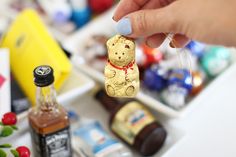 a person holding up a gold teddy bear ornament in front of some liquor bottles