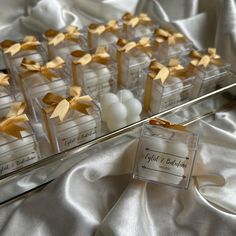 small clear boxes with gold bows are sitting on a white satin tablecloth, next to some candles