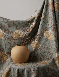 a vase sitting on top of a table next to a wallpaper covered with a curtain