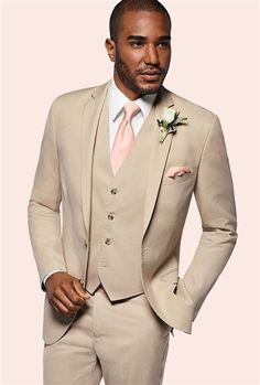 a man in a tan suit with a pink tie and flower on his lapel