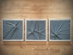 three square paintings are displayed on a wooden surface, one is gray and the other is white