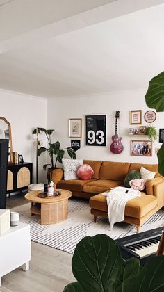 a living room filled with lots of furniture and plants on the wall above it is a piano