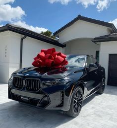 a black car with a large red bow on it's hood parked in front of a house