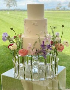 a three tiered cake with flowers in the middle on a table outside by some grass