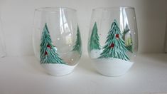 two wine glasses decorated with christmas trees on white counter top next to eachother