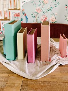 three books sitting on top of a wooden floor next to a wallpapered wall