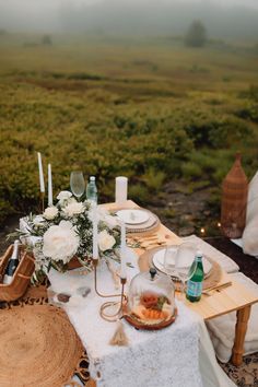 a table set up with candles, plates and flowers in the middle of an open field