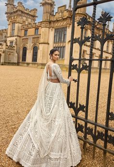 a woman standing in front of a gate wearing a long white dress with an open back