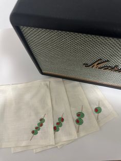 four napkins with embroidered cherries on them sitting next to an old fashioned radio