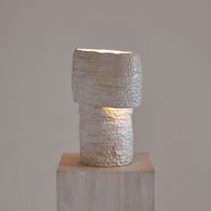 a white vase sitting on top of a wooden block with a light shining through it