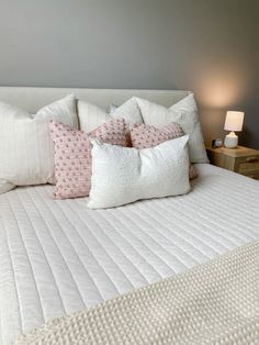 a white bed topped with lots of pillows next to a night stand and table lamp