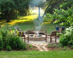 a fire pit surrounded by wooden chairs in the middle of a yard with grass and trees