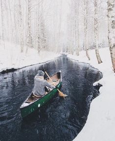 a person in a green canoe paddling down a river with snow on the ground