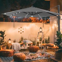 an outdoor patio is lit up with string lights and blankets on the floor, surrounded by potted plants