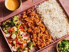 a tray filled with rice, meat and veggies next to dipping sauces