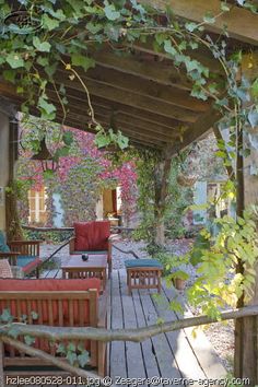 an outdoor covered patio with wooden furniture and greenery on the roof, surrounded by pink flowers