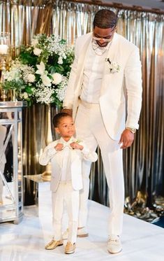 a man in a white suit standing next to a little boy