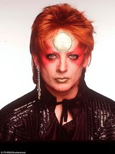 a man with red hair and piercings on his forehead wearing a black shirt, earrings and headpiece