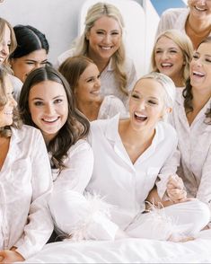 a group of beautiful women sitting next to each other on top of a white bed